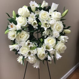 White floral wreath on a black stand with roses and lilies