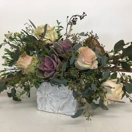 Low floral arrangement with roses, succulents, and greenery in a white vase
