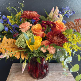 Mixed bouquet of roses, chrysanthemums, and blue flowers in a red glass vase