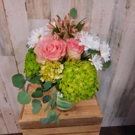 Pink roses with white daisies and green hydrangeas in a striped vase