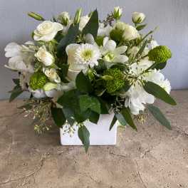 White floral arrangement in a square vase with green accents