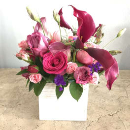 Pink and magenta floral arrangement in a white square vase