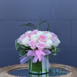 Pink and white roses arranged in a glass vase with a pink ribbon