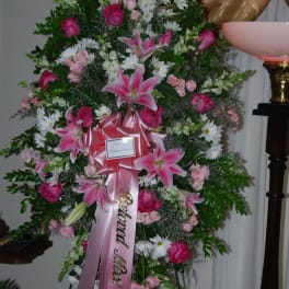 Tall standing floral spray with pink lilies and roses on a ribboned easel