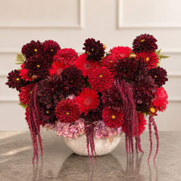 Red and burgundy flower arrangement in a white bowl vase