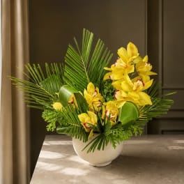 Yellow orchids arranged in a white bowl vase with palm fronds