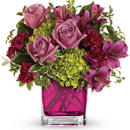 Pink roses and magenta flowers arranged in a square glass vase