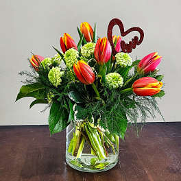 Short vase arrangement of orange tulips and green button flowers with a red glitter heart pick