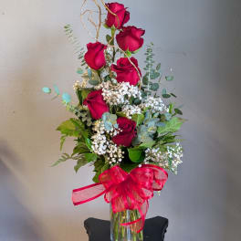 Tall bouquet of red roses in a glass vase with a red ribbon