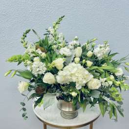 White floral arrangement in a silver vase with green accents