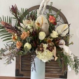 Large mixed floral arrangement in a tall white vase with white anthuriums and roses