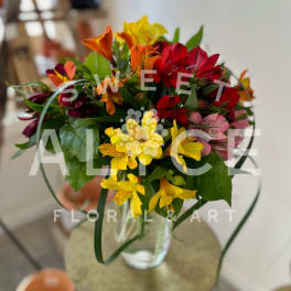 Mixed bouquet of red, yellow, orange, and pink flowers in a clear glass vase