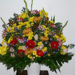 Large mixed flower arrangement in a white vase with red, yellow, and purple blooms