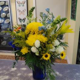 Mixed bouquet with yellow chrysanthemums, white roses, blue flowers, and lilies in a blue vase