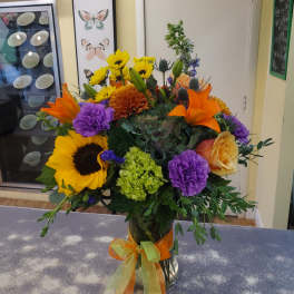 Colorful mixed bouquet in a glass vase with sunflowers, lilies, and roses