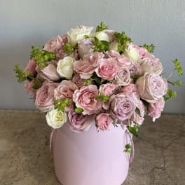 Pink and white roses arranged in a round pastel pink box
