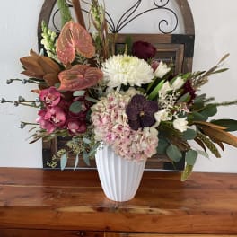 Mixed floral arrangement in a white vase with pink, white, and burgundy blooms