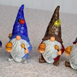 Set of four colorful gnome figurines holding honey pots with bees and a ladybug on their tall textured hats.