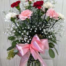 Pink and red carnations in a glass vase with a pink ribbon