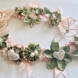 Money lei with pink ribbon and paper flowers on a white surface