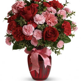 Red and pink flower arrangement in a red vase with a pink ribbon