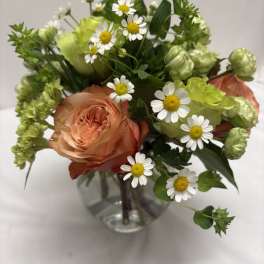 Small arrangement of peach roses and white daisies in a round glass vase.