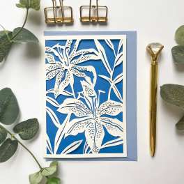 Blue floral cutout card with white lily design and a gold pen