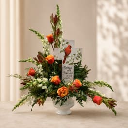 Orange roses in a white vase with a memorial card and cardinal design