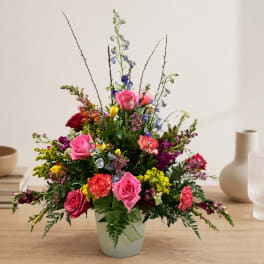 Mixed bouquet of roses, carnations, and snapdragons in a pale vase