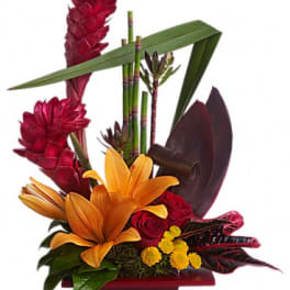 Tropical floral arrangement with orange lilies, red blooms, and bamboo in a red container