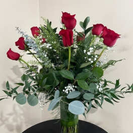 Tall arrangement of long-stem red roses with white filler flowers in a clear glass vase