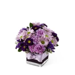 Lavender and purple bouquet in a square glass vase with a ribbon