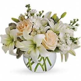 Low arrangement of white lilies and cream roses in a clear round vase with visible crisscrossed stems