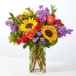 Mixed bouquet with sunflowers, roses, and purple flowers in a glass vase