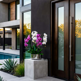 Purple and white orchids in a silver pot on a pedestal outside a modern house