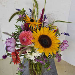 Mixed bouquet with sunflowers, pink blooms, and purple flowers in a glass vase