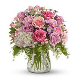 Pink and lavender rose arrangement with white hydrangea and asters in a clear glass vase
