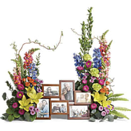 Two tall colorful floral arrangements framing a wooden multi-photo picture frame display.
