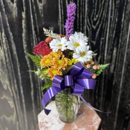 Bouquet of mixed flowers in a glass vase with a purple ribbon