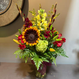 Mixed bouquet with a sunflower, red blooms, and yellow snapdragons in a glass vase