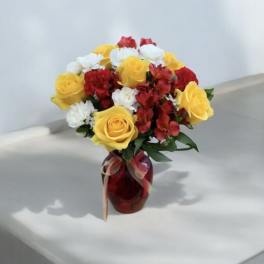 Bouquet of yellow roses, red flowers, and white blooms in a red vase