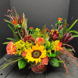 Mixed bouquet with a sunflower, roses, and orange blooms in a patterned container