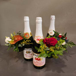Three sparkling cider bottles arranged with flowers and greenery