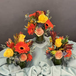 Three small floral arrangements in green vases with yellow and orange blooms