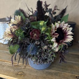 Dark floral arrangement in a gray vase with sunflowers and burgundy blooms
