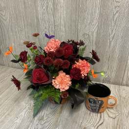 Halloween floral arrangement in an orange container with a matching mug beside it