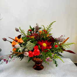 Mixed bouquet in a copper pedestal vase with red, orange, and pink flowers