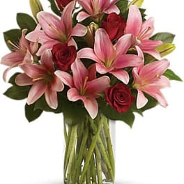 Pink lilies and red roses arranged in a clear glass vase