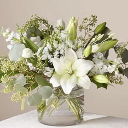 White lilies and greenery arranged in a clear glass vase