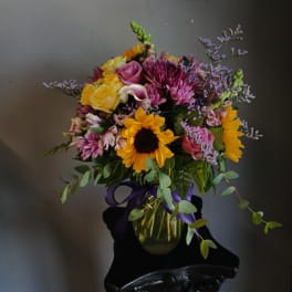 Mixed bouquet with sunflowers, roses, and purple flowers in a glass vase